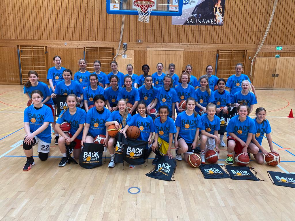 Gruppenbild Mädchen in blauen Shirts und mit schwarzen Turnbeuteln vor dem Korb