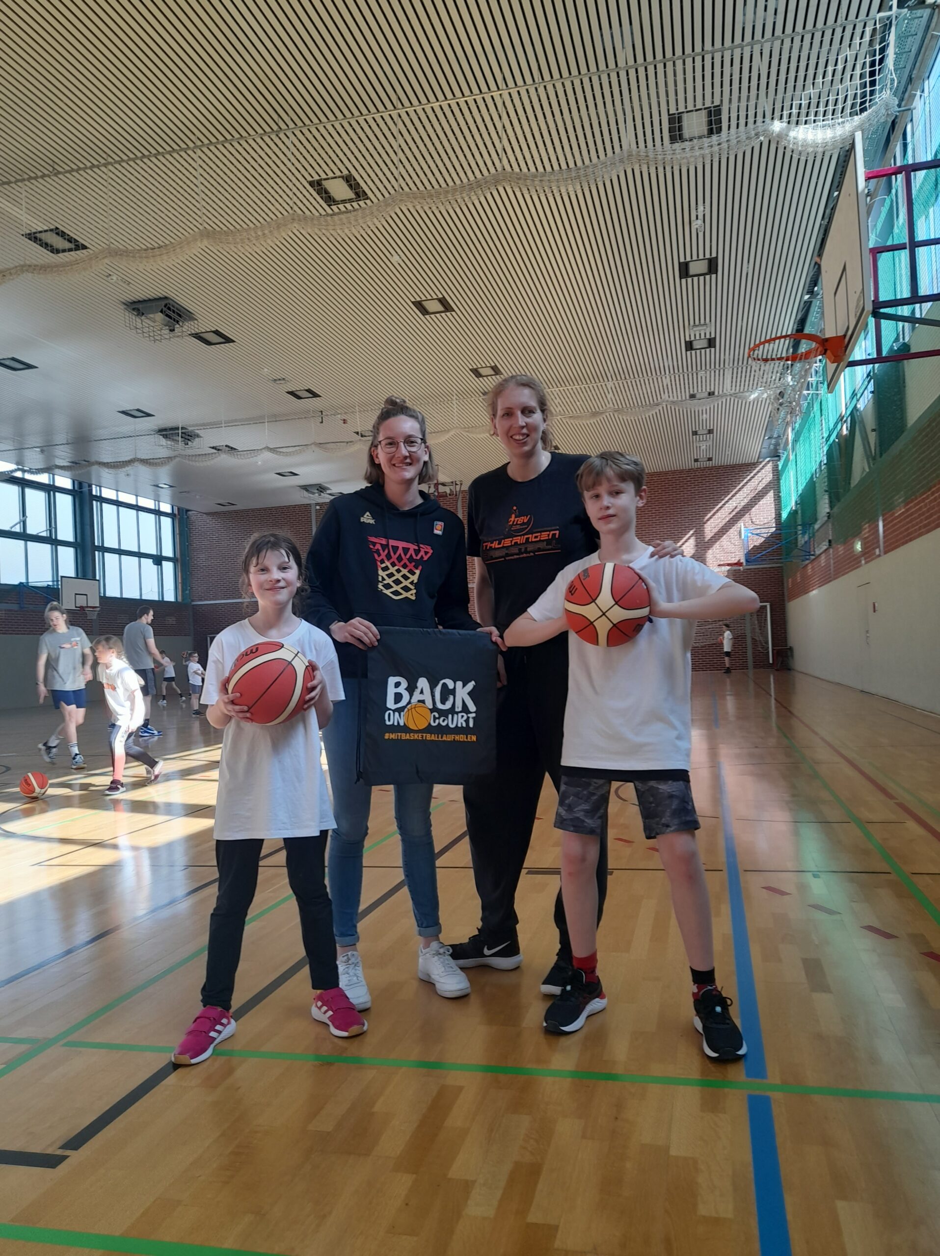 zwei Kinder mit Ball in der Hand posieren zusammen mit der Aufbaumanagerin und der Landestrainerin